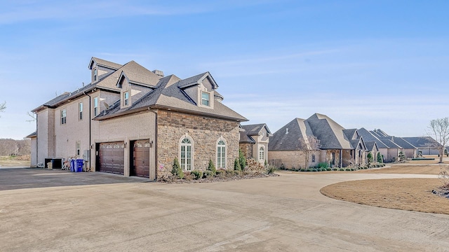 view of side of property with driveway, stone siding, a garage, and cooling unit