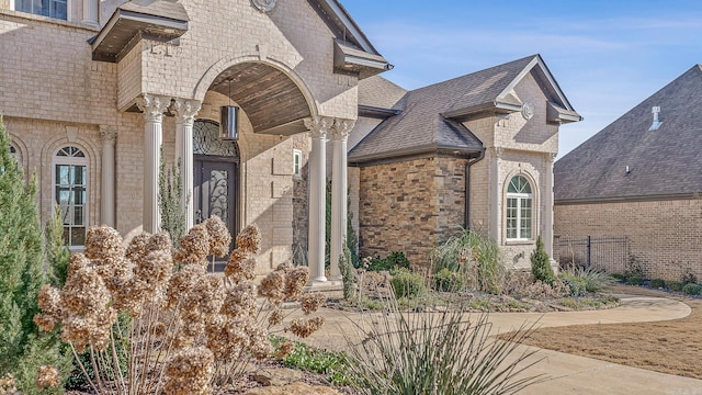 doorway to property with stone siding, brick siding, and roof with shingles