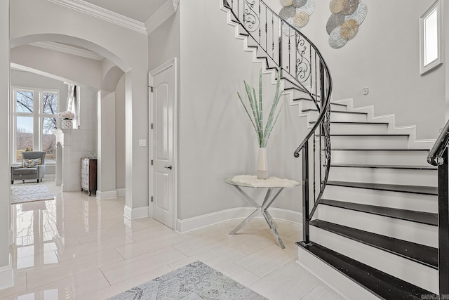 entryway with arched walkways, stairway, baseboards, and crown molding