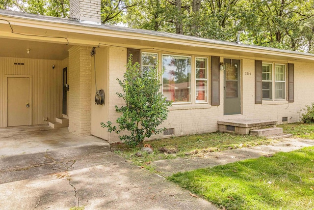 property entrance with crawl space, driveway, a chimney, and brick siding