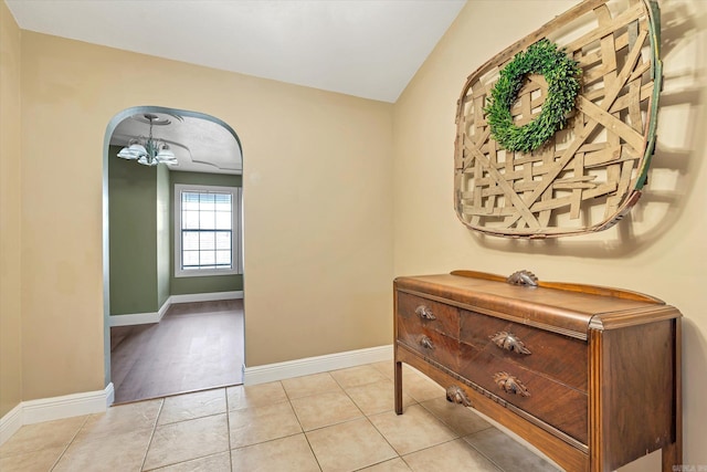 hallway featuring an inviting chandelier, baseboards, arched walkways, and light tile patterned flooring