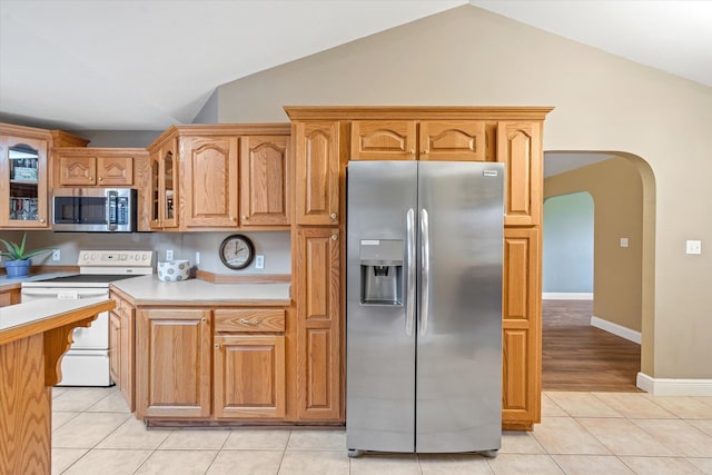 kitchen featuring arched walkways, light tile patterned floors, stainless steel appliances, light countertops, and glass insert cabinets