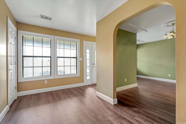 foyer featuring arched walkways, a textured ceiling, wood finished floors, visible vents, and baseboards