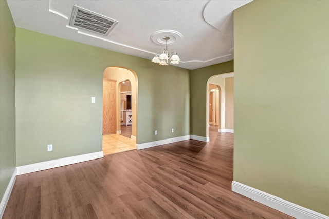 unfurnished room featuring baseboards, visible vents, arched walkways, and wood finished floors