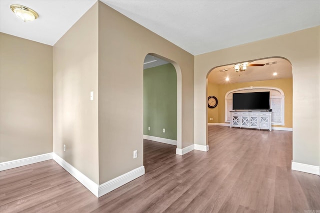 unfurnished room featuring arched walkways, wood finished floors, and baseboards