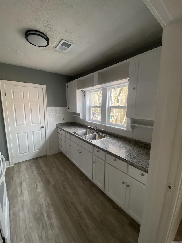 kitchen with dark wood finished floors, visible vents, white cabinets, a sink, and a textured ceiling