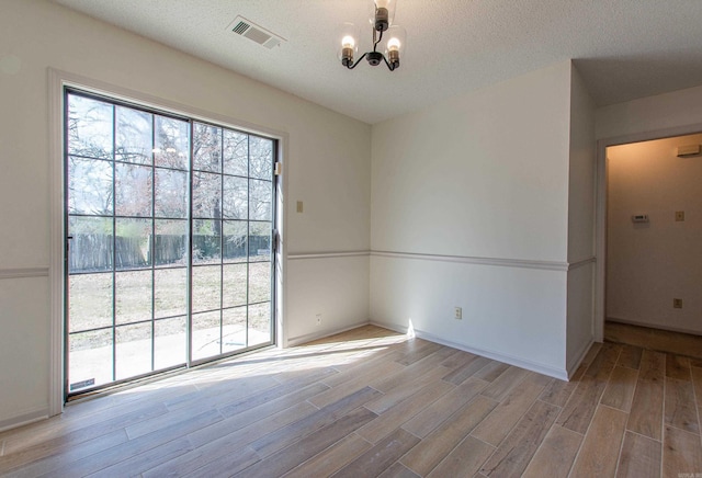 empty room with a textured ceiling, wood finished floors, visible vents, and a notable chandelier