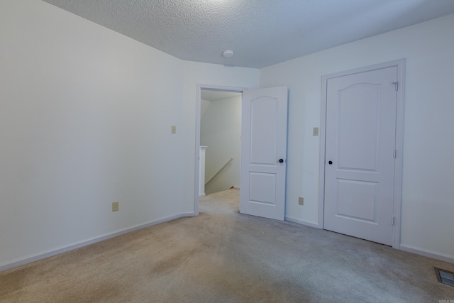 unfurnished bedroom with a textured ceiling, baseboards, visible vents, and light colored carpet