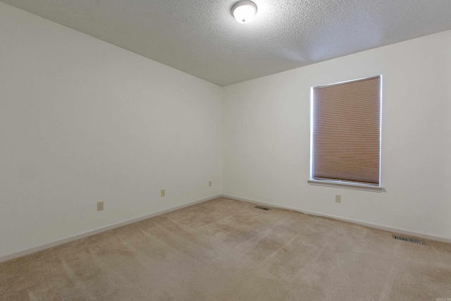 spare room featuring a textured ceiling, baseboards, visible vents, and light colored carpet