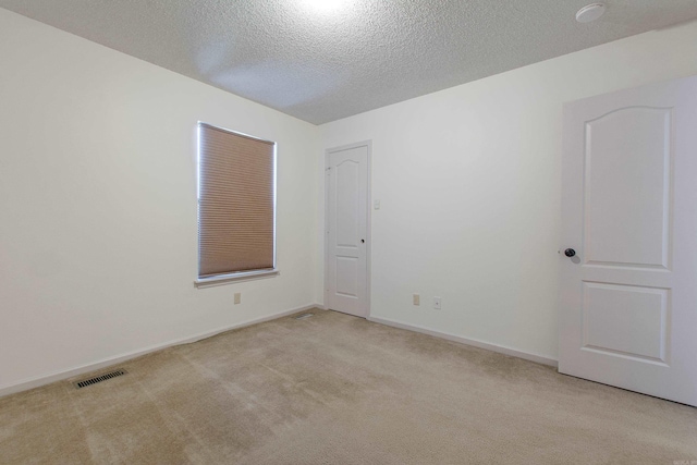 empty room with light colored carpet, visible vents, a textured ceiling, and baseboards