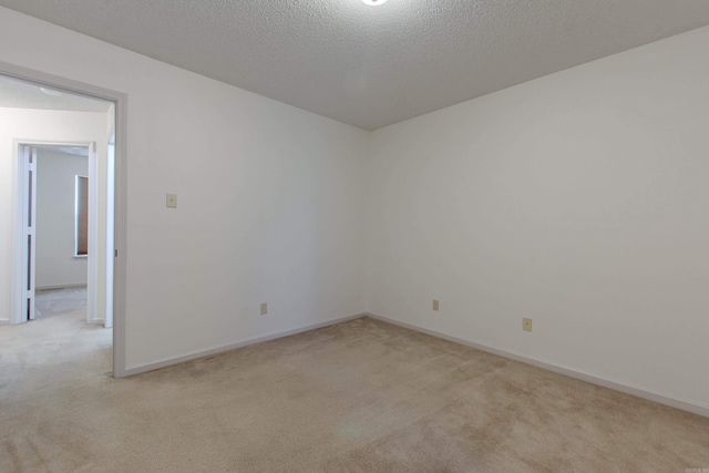 spare room featuring light carpet, a textured ceiling, and baseboards