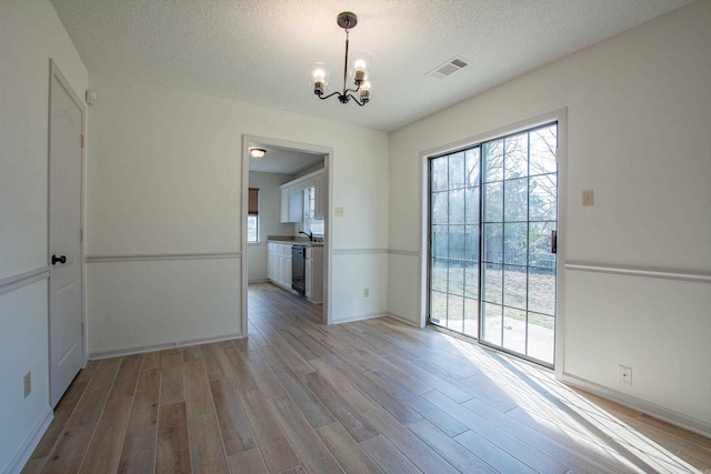 unfurnished dining area with light wood-style floors, a textured ceiling, visible vents, and a notable chandelier