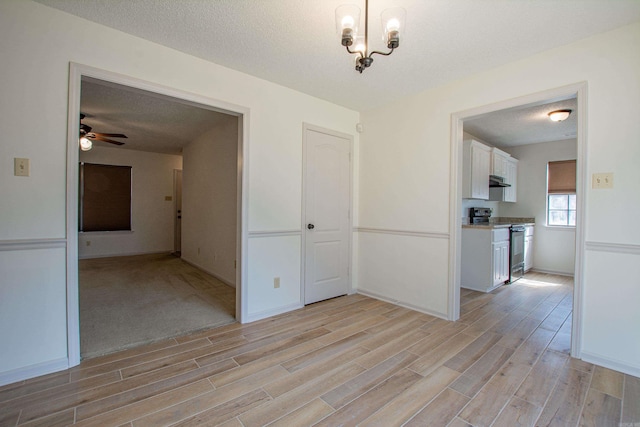 unfurnished dining area with a ceiling fan, light wood-type flooring, a textured ceiling, and baseboards