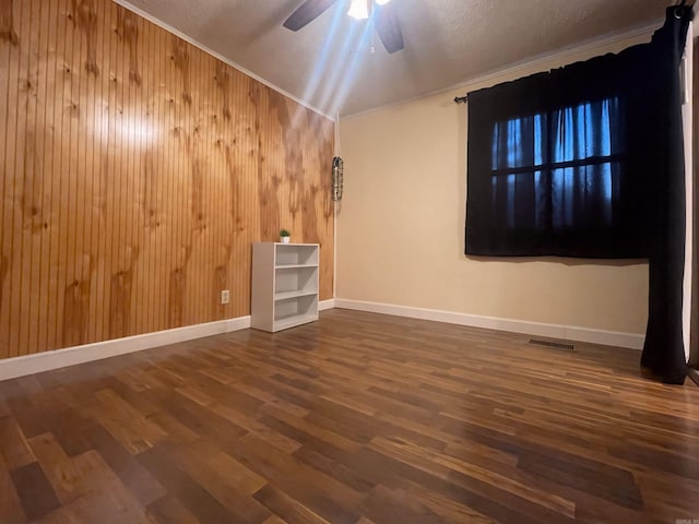 empty room with baseboards, dark wood-style floors, ceiling fan, crown molding, and wood walls