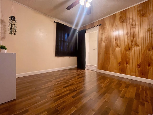 spare room with a ceiling fan, crown molding, wood walls, and wood finished floors