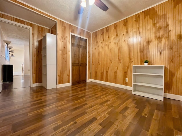 spare room featuring ornamental molding, wood walls, ceiling fan, wood finished floors, and baseboards