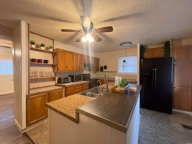 kitchen featuring a sink, black fridge, brown cabinetry, stainless steel microwave, and an island with sink