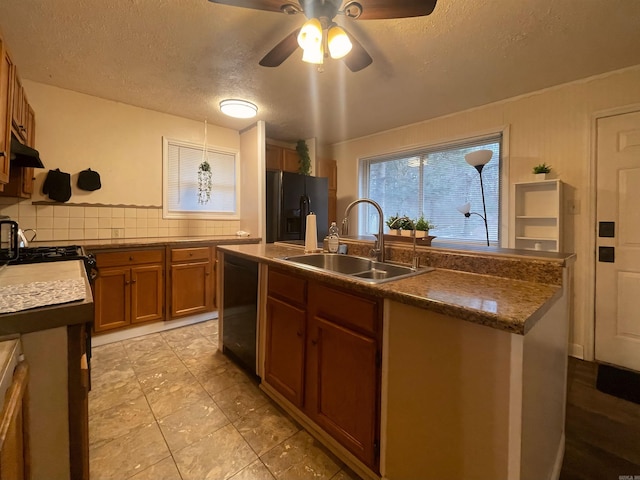 kitchen with a kitchen island with sink, a sink, brown cabinets, decorative backsplash, and black appliances