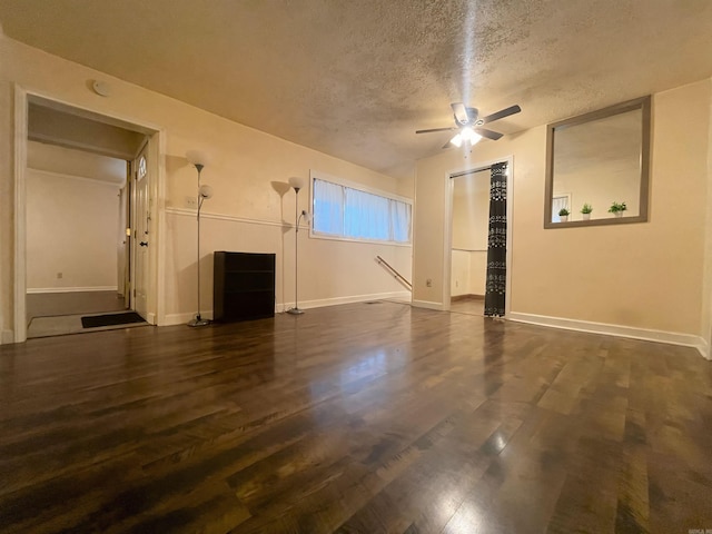 unfurnished living room featuring a ceiling fan, dark wood-style flooring, a textured ceiling, and baseboards