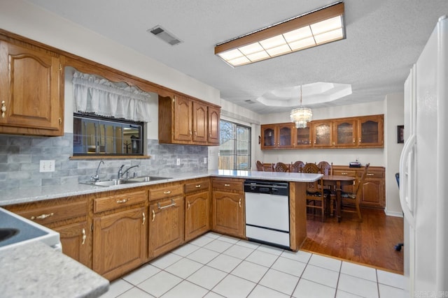 kitchen featuring a peninsula, white appliances, a sink, visible vents, and brown cabinetry