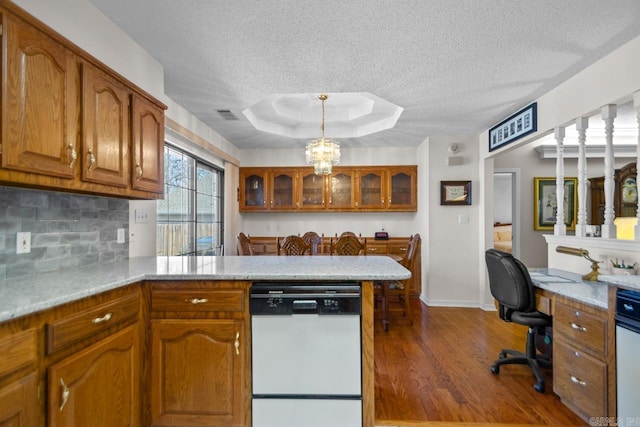 kitchen with a raised ceiling, brown cabinets, white dishwasher, and a peninsula