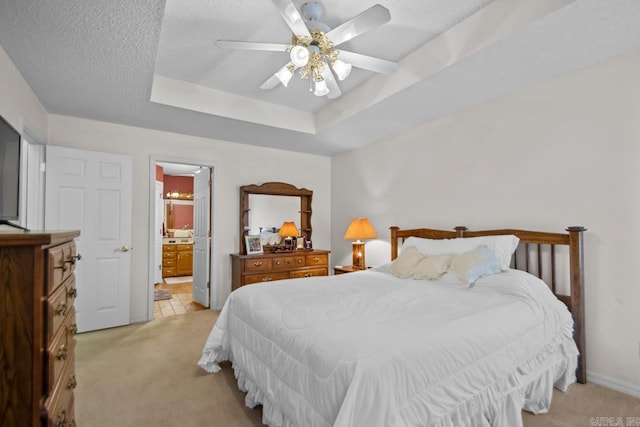 bedroom with light carpet, a tray ceiling, a textured ceiling, and connected bathroom