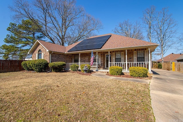 ranch-style home with covered porch, brick siding, fence, and roof mounted solar panels