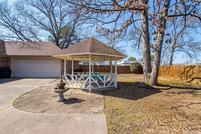 exterior space featuring an attached garage, driveway, a gazebo, and fence