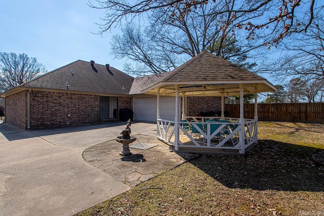 exterior space with a garage, brick siding, a shingled roof, fence, and concrete driveway