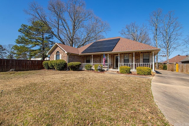 ranch-style house with covered porch, a front lawn, fence, and roof mounted solar panels