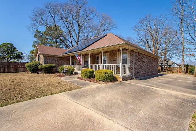 single story home with covered porch, brick siding, fence, roof mounted solar panels, and a front lawn