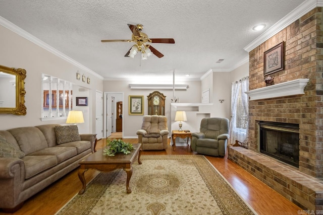 living area featuring a textured ceiling, a fireplace, wood finished floors, a ceiling fan, and ornamental molding