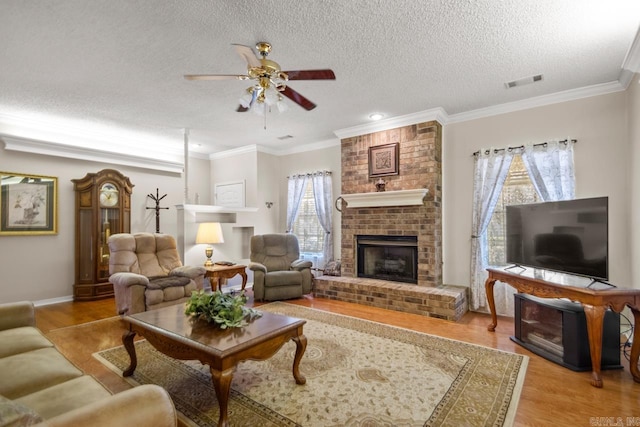 living room featuring a brick fireplace, wood finished floors, visible vents, and crown molding