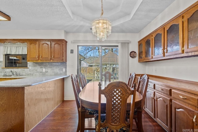 dining space featuring a chandelier, a tray ceiling, a textured ceiling, and dark wood finished floors