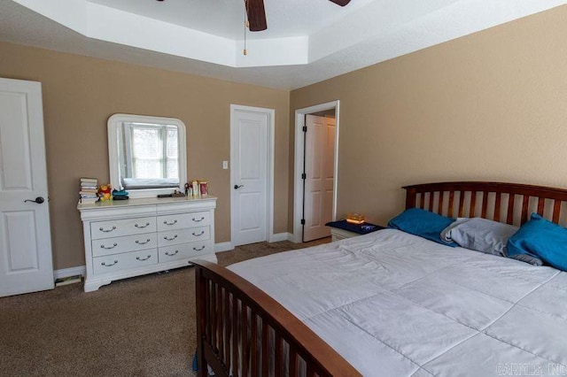 carpeted bedroom with a raised ceiling, a ceiling fan, and baseboards