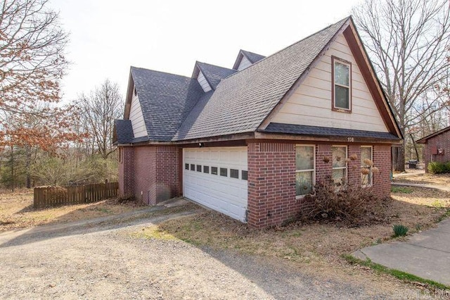 view of side of property with a garage, driveway, brick siding, and roof with shingles