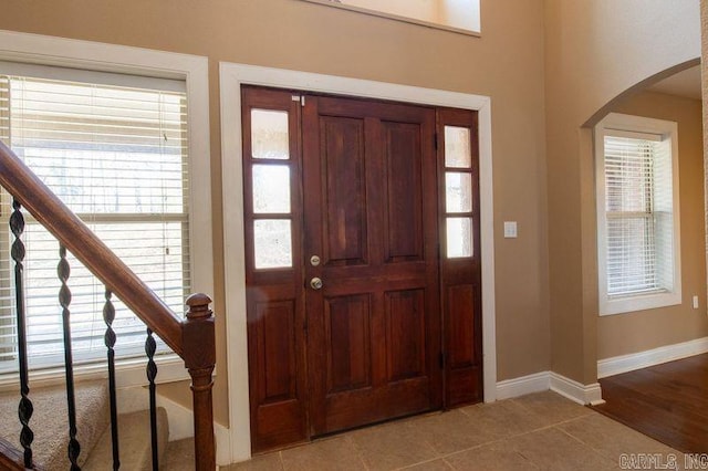 tiled entrance foyer featuring arched walkways, stairway, and baseboards