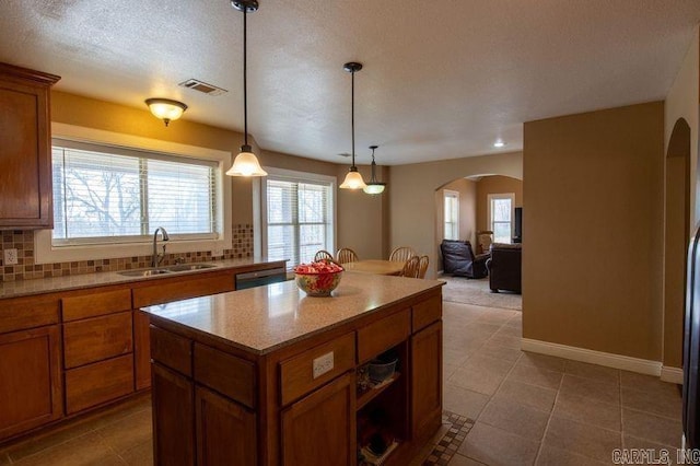 kitchen with arched walkways, backsplash, a sink, and brown cabinetry