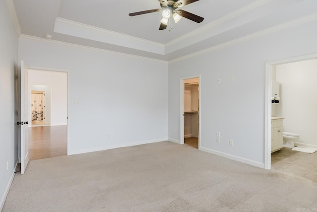 unfurnished bedroom with light carpet, a tray ceiling, a walk in closet, and crown molding