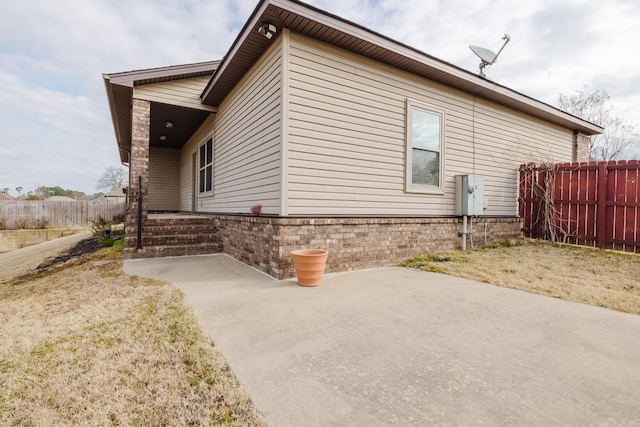 view of side of home with a patio area, fence, and brick siding