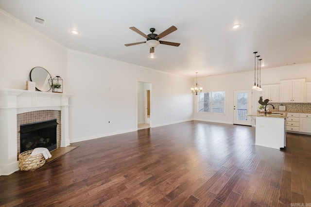 unfurnished living room featuring ceiling fan with notable chandelier, dark wood-type flooring, a fireplace, a sink, and visible vents