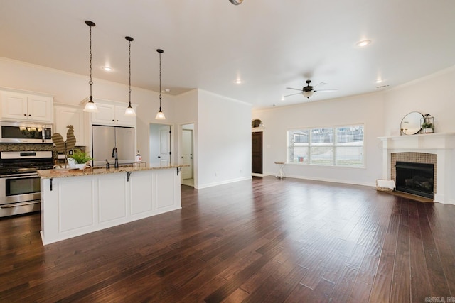 kitchen with light stone counters, dark wood-style floors, a tiled fireplace, appliances with stainless steel finishes, and open floor plan