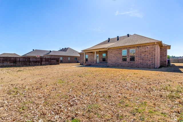 back of house featuring brick siding, fence, and a lawn