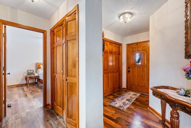 foyer entrance featuring a textured ceiling, dark wood finished floors, and baseboards