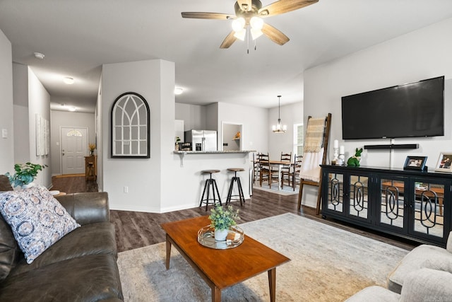 living room with baseboards, dark wood-type flooring, and ceiling fan with notable chandelier