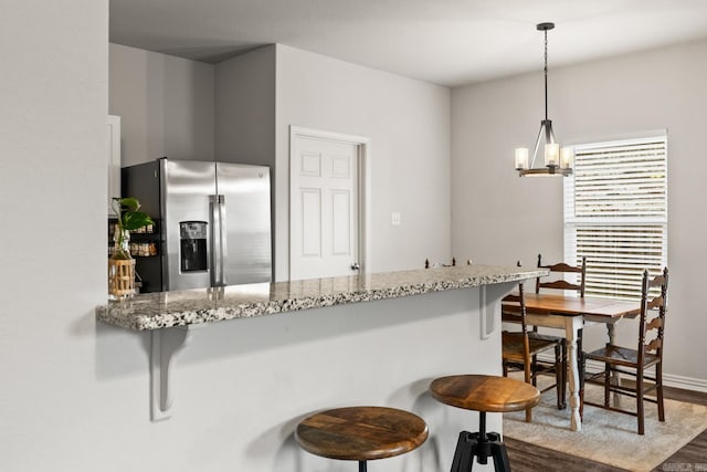 kitchen with dark wood-type flooring, a peninsula, light stone countertops, a chandelier, and stainless steel refrigerator with ice dispenser