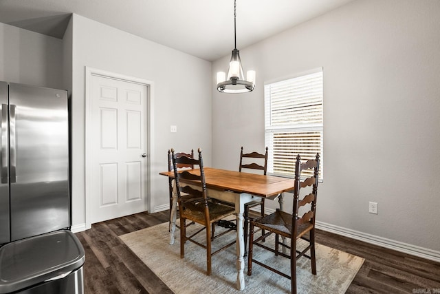 dining area with dark wood-type flooring, a notable chandelier, and baseboards