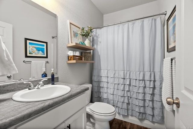 full bath featuring a textured wall, wood finished floors, vanity, and toilet