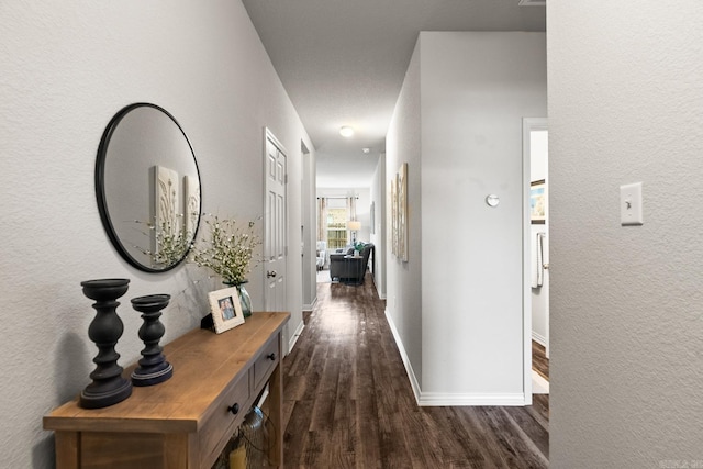 hallway featuring dark wood-style floors, a textured wall, and baseboards