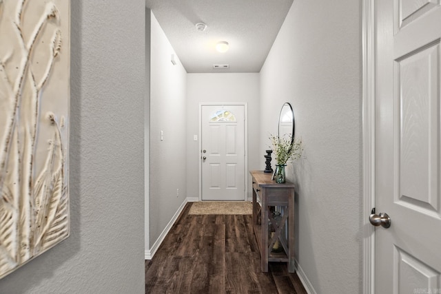 doorway with visible vents, baseboards, a textured wall, dark wood-style floors, and a textured ceiling